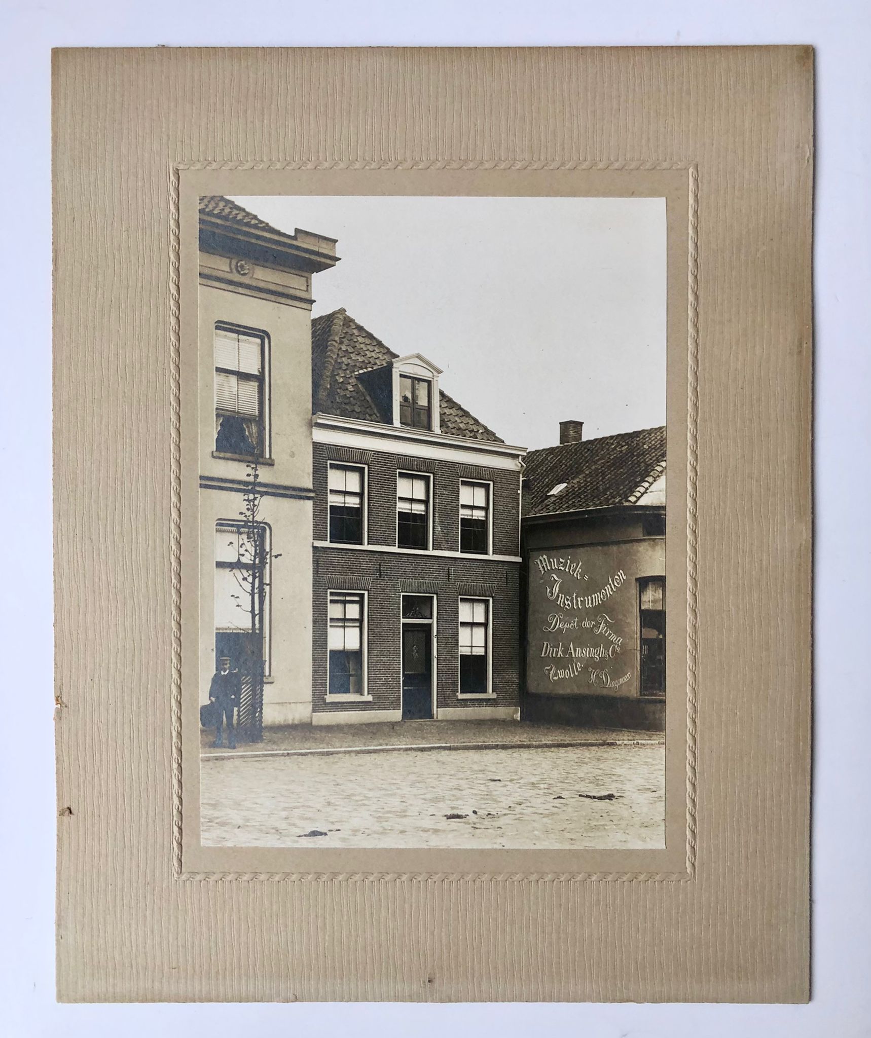 [Photography, Enschede, 1920?] Photography of a house, 17x12 cm., with on the wall of the neighbour text 'muziek-instrumenten'. Depot der firma Dirk Ansingh and Co, Zwolle, H. Deegenaar.', ca. 1920?